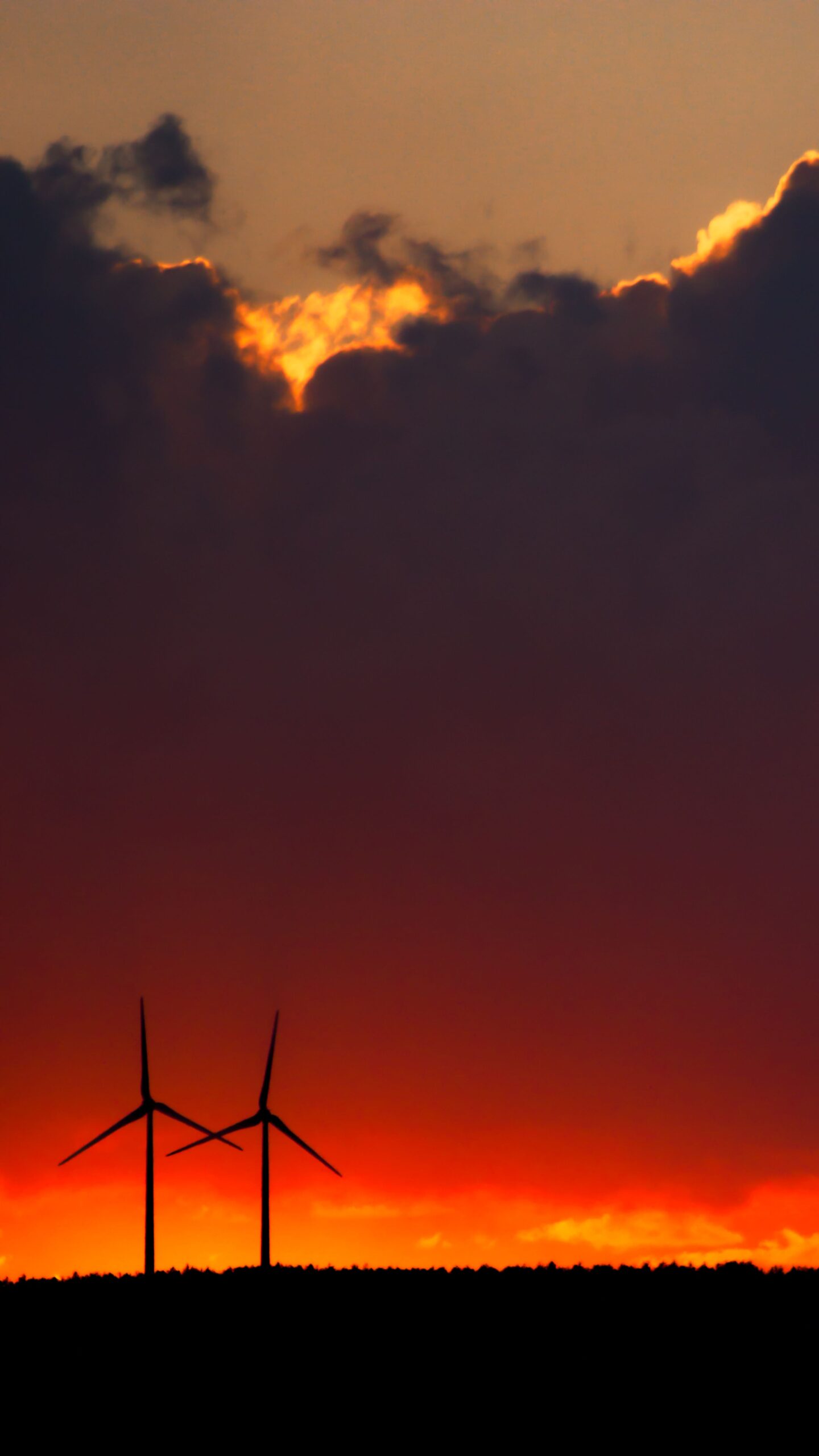 Silhouette of wind turbines against a dramatic sunset sky with vibrant colors and cloud formations.